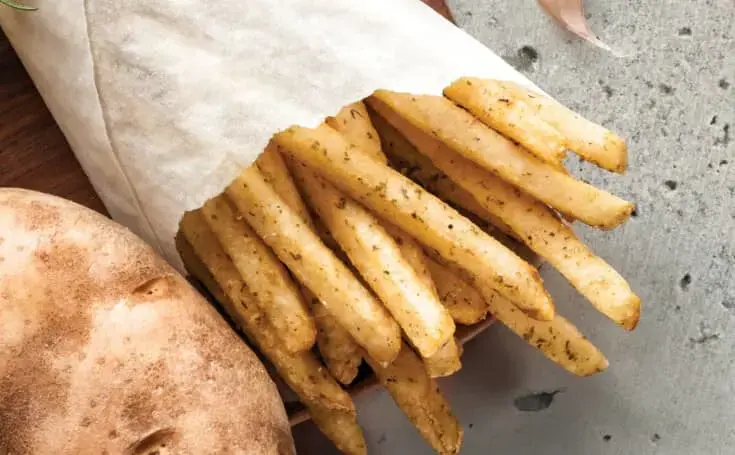 A corner of a raw potato next to a bag of fries